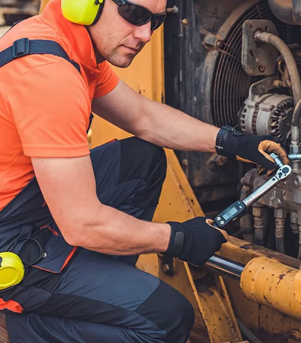 Mechanik serwisuje maszynę budowlaną kluczem dynamometrycznym.